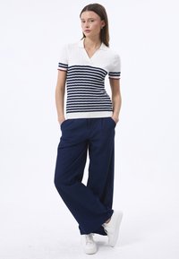 Polo en tricot à manches courtes de couleur blanche avec des rayures horizontales bleu marine et des accents rouges, associé à un pantalon ample bleu marine et des baskets blanches.