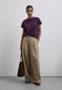Paarse katoenen T-shirt met korte mouwen, gecombineerd met beige, high-waisted, broek met wijde pijpen. Accessoires zijn onder andere een bruine schoudertas.