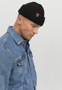 Must have mustreeritud must müts, millel on ribakonstruktsioon ja väike roheline ja punane lapik, kantud sinise teksajaki koos nööpide ja taskutega.