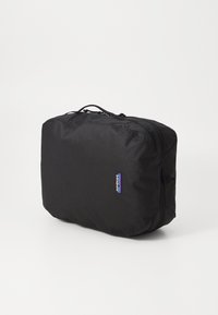 Svart rektangulær pakkebolle laget av slitesterkt stoff, med glidelås og en liten logo på siden, designet for organisering på reise.