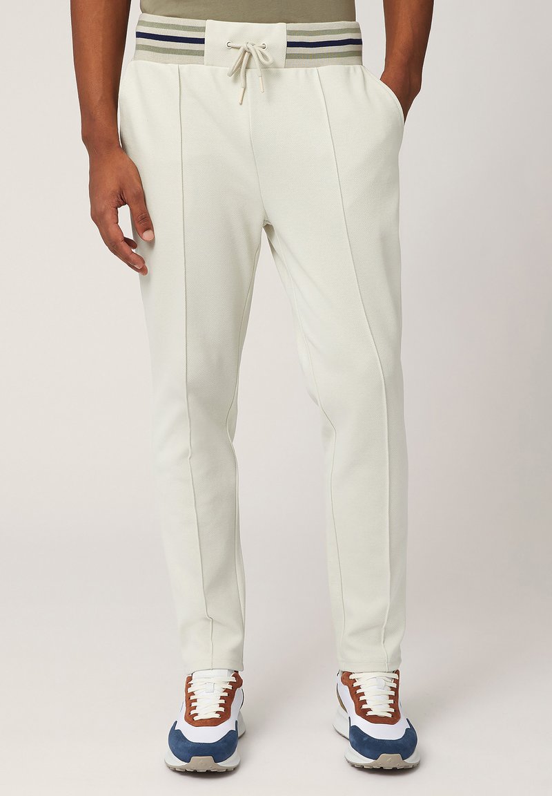 Lichtgrijze joggingsbroek met een contrasterende gestreepte elastische tailleband, voorzien van zijzakken en taps toelopende benen. Zacht, gestructureerd materiaal.