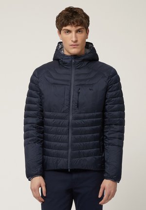 Marineblauwe pufferjack met capuchon, voorzien van een ritssluiting en een slim fit. Horizontaal gequilte patroon met een borstzak en elastische manchetten.
