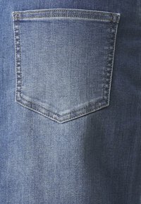 Denim hlače imajo en sam zadnji žep s koničasto pokrivalo, v srednji modri pranju z rahlo teksturirano površino in vidnim šivanjem.