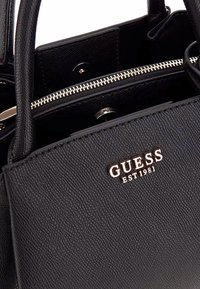 Borsa nera realizzata in pelle textured con doppi manici, chiusura a zip e logo dorato sul davanti. Interno foderato.
