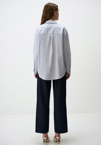 Camicia a righe blu chiaro con una vestibilità comoda, maniche lunghe e orlo arrotondato, abbinata a jeans larghi scuri e décolleté beige.