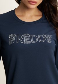 Camisa de manga larga azul marino hecha de tejido suave que presenta la palabra "FREDDY" en brillantes strass en el pecho.