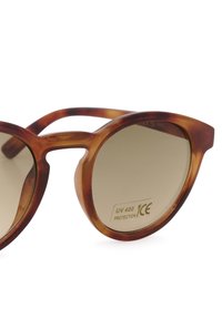 Lunettes de soleil écaille de tortue marron avec monture ronde, verres dégradés et marquage CE, offrant une protection UV 400. Surface texturée sur la monture.