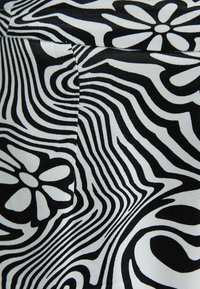 Svart och vit tyg med abstrakta vågiga linjer och stora blommönster, där en synlig söm och veck syns.