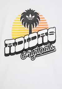 Balta T-kreklu ar grafisku dizainu, kas attēlo palmu un oranždzeltenus saulrieta strīdus, uz kura ir bieza melna fontā rakstīts "ADIDAS Originals".