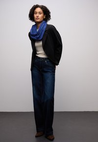 Tmavě modré džíny s vysokým pasem, krémový top, černé sako a modrý šátek. Součástí jsou strukturované sako, džíny s širokými nohavicemi a kotníkové boty.