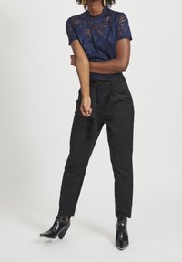 Marinblus med korta ärmar, kombinerad med högmidjade svarta byxor och glänsande svarta ankelskor. Elegant design och figursydd silhuett.