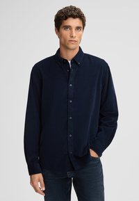 Marineblaues Hemd mit Knöpfen aus weichem Stoff, mit Kragen, langen �Ärmeln und einer entspannten Passform, kombiniert mit dunklen Jeans.