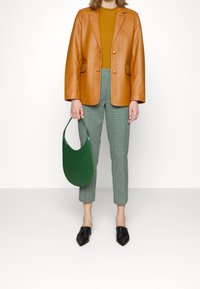 Bruine leren blazer, mosterdkleurige top, groen geruite broek, groene handtas en zwarte puntige schoenen. Strakke lijnen en gestructureerde pasvorm.