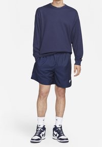 Námořnické triko s dlouhým rukávem a žebrováním kombinované s námořnickými kraťasy s elastickým pasem. Obuto s bílými ponožkami Nike a teniskami.