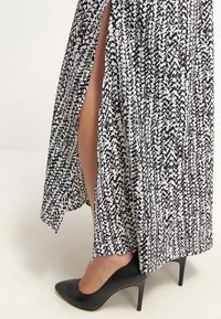 Maxiklänning med ett svart-vitt abstrakt mönster, med sidoklyftor och en lätt tyg. Svart högklackssko delvis synlig.