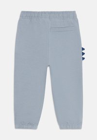 Pantalon de survêtement pour tout-petit bleu clair avec taille et poignets élastiques, une poche arrière passepoilée et des pics de dinosaure bleus sur le côté.