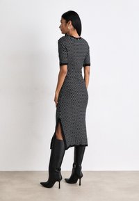 Black and white patterned knit dress with short sleeves, side slits, and a fitted silhouette, paired with knee-high black heeled boots.
