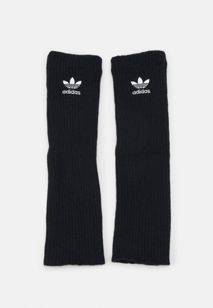Fekete bordázott lábmelegítők puha anyagból, fehér Adidas logóval és a híres három csíkkal a tetején.