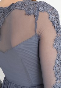 Grå klänning med en figurnära bodice och ett nätöverlägg på axlarna samt intrikata spetsdetaljer som sömlöst kombinerar texturer och mönster.