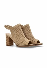 Sandalias de ante perforadas color beige con puntera abierta, diseño tipo slingback y acento de herrajes circulares. Tacones cuadrados texturizados.