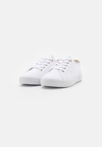 Sneakers bianchi in tela con lacci piatti, occhielli in metallo dorato, suola in gomma testurizzata e punta rigata. Design semplice con branding minimale.