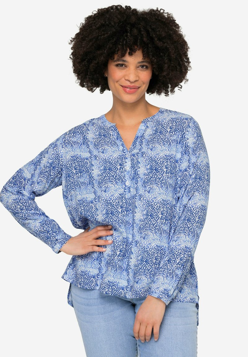 Blusa azul estampada con cuello en V, cierre de botones en la parte delantera y mangas largas. Presenta un ajuste holgado y aberturas laterales, fabricada en un tejido ligero.