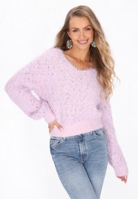 Flauschiger, hellvioletter Pullover mit bunten Sprenkeln, weitem Ausschnitt und gerippten Bündchen und Saum; kombiniert mit hellblauen Jeans.