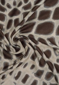 Materiał w wzór żyrafy w odcieniu beżowym z nieregularnymi, ciemnobrązowymi plamami, charakteryzujący się miękką, zwiewną teksturą, która układa się gładko.