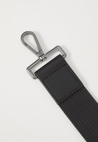 Black nylon strap with a matte finish, featuring a metallic clip and leather accents, showcasing distinct stitching and durable material.