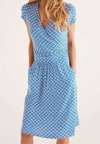 Blå omlottklänning med ett upprepat vitt vågmönster, korta ärmar, insvängd midja och fickor på båda sidor.