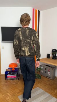 El suéter presenta una base marrón oscura con patrones de pinceladas claras en contraste. Jeans oscuros de corte holgado. Fondo interior minimalista.