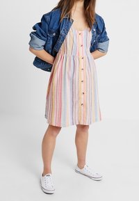 Vestito estivo a righe in colori pastello, con una chiusura a bottoni frontale, tessuto morbido e una silhouette svasata, abbinato a una giacca di jeans.