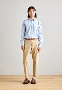 Chemise bleu clair à manches longues, pantalon beige, chaussures marron. La chemise a un col, tandis que le pantalon est effilé. Textures lisses, design simple.