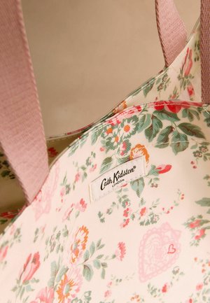 Torba na ramię w kwiaty ma jasne, materiałowe wnętrze ozdobione różowymi, zielonymi i pomarańczowymi kwiatami. Zawiera metkę marki.