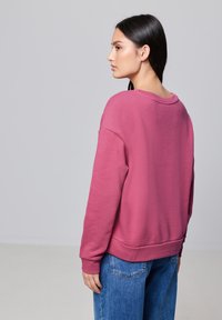 Sweatshirt en polaire rose, avec une coupe décontractée, des poignets et un ourlet côtelés. Assorti à un jean en denim bleu. Texture lisse et design décontracté.