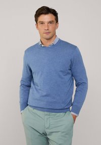 Blauw ronde hals trui gemaakt van lichtgewicht gebreide stof. Heeft lange mouwen en geribde manchetten, gecombineerd met lichtgroene broek eronder.