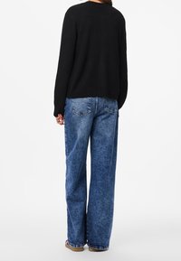 Suéter negro de punto con mangas largas, combinado con jeans de mezclilla azul de pierna ancha que presentan un lavado descolorido y bolsillos traseros.