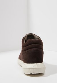 Baskets en daim marron avec col rembourré et semelle blanche tachetée, vues de dos sur un fond blanc uni.