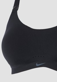 Czarny sportowy stanik z gładkiego materiału, szerokimi ramiączkami i szarym logo Nike. Posiada subtelne otwory wentylacyjne w pobliżu pasa.