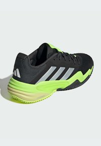Zapatilla deportiva negra con parte superior de malla texturizada, acentos plateados y una suela verde brillante. Cuenta con una mediasuela acolchada y una suela exterior duradera.