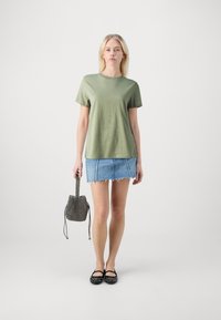 Olijfgroene t-shirt, denim mini rok met rafelige zoom, zwarte studded flats en een gestructureerde zwarte bucket bag. Eenvoudige, casual outfit.