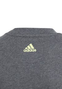 Szara bawełniana koszulka z okrągłym dekoltem. Posiada subtelną teksturę oraz limonkowe logo Adidas na plecach.
