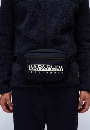 Giacca in pile blu navy con zip a metà, abbinata a una marsupio blu navy con logo bianco. Tessuto morbido e texturizzato con cinturino regolabile.