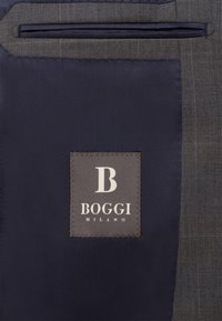 Jūras spēku auduma iekšpuse ar pelēku skotu rakstu. Ietver kvadrāta formas logo etiķeti ar "B BOGGI MILANO" sudraba burtiem. Gluda tekstūra.