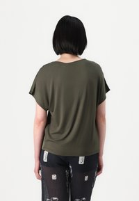 Maglietta verde oliva a maniche corte con una vestibilità comoda e scollatura rotonda. Tessuto morbido e liscio con una leggera caduta. Indossata con pantaloni neri a motivi.