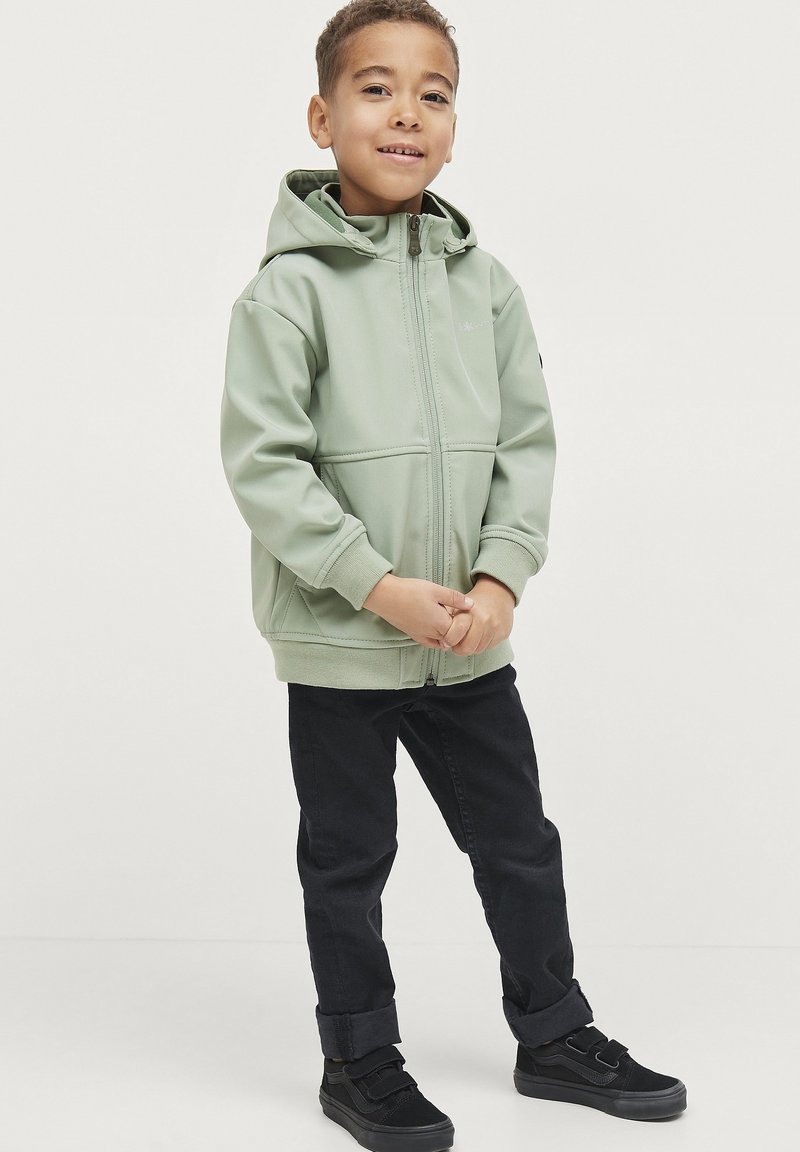 Lys grøn zip-up hoodie med hætte, der har elastiske manchetter og kant. Sammen med sorte opsmøgede bukser og sorte sneakers med velcroremme.