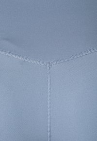 Vaaleansiniset legginsit, jotka on valmistettu sileästä ja elastisesta kankaasta, sisältävät keskilinjan ja litteät saumat mukavuutta ja istuvuutta varten.