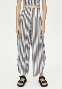 Zwart-witte gestreepte brede broek met hoge taille, zijsplitten en een zachte, textuurrijke stof. Gecombineerd met zwarte sandalen.
