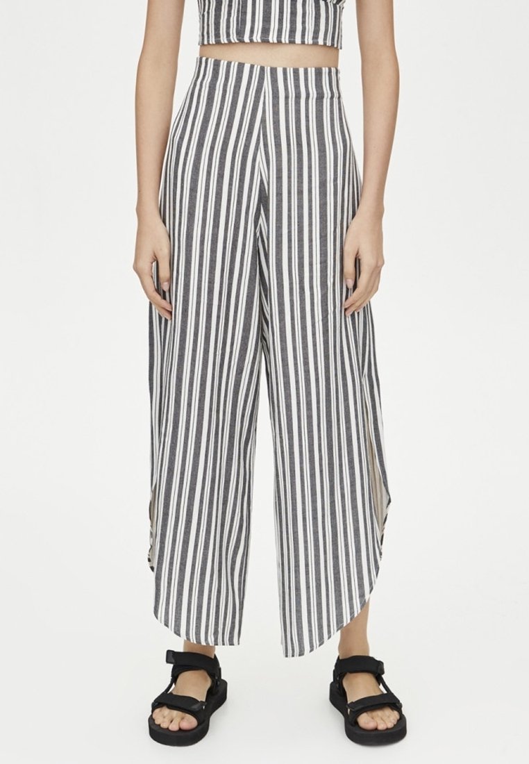 Zwart-witte gestreepte brede broek met hoge taille, zijsplitten en een zachte, textuurrijke stof. Gecombineerd met zwarte sandalen.