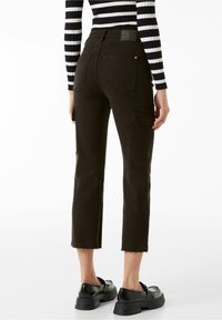 Svarta cropped cargobyxor med fransad nederkant, som har två sidofickor, en figursydd midja och en lapp bak. Slätt bomullstyg.